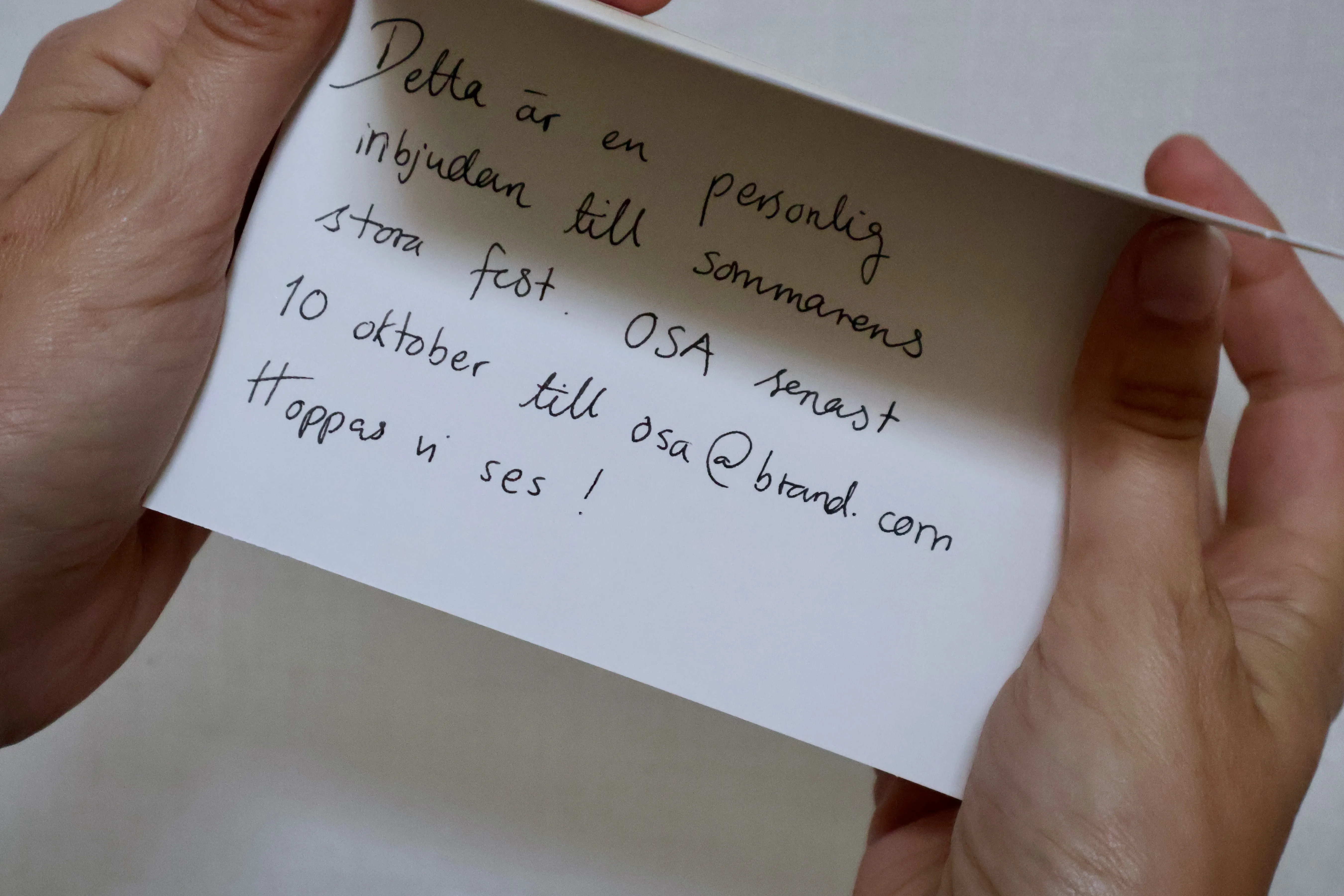 Händer som håller ett öppet vikt kort med handskriven inbjudan